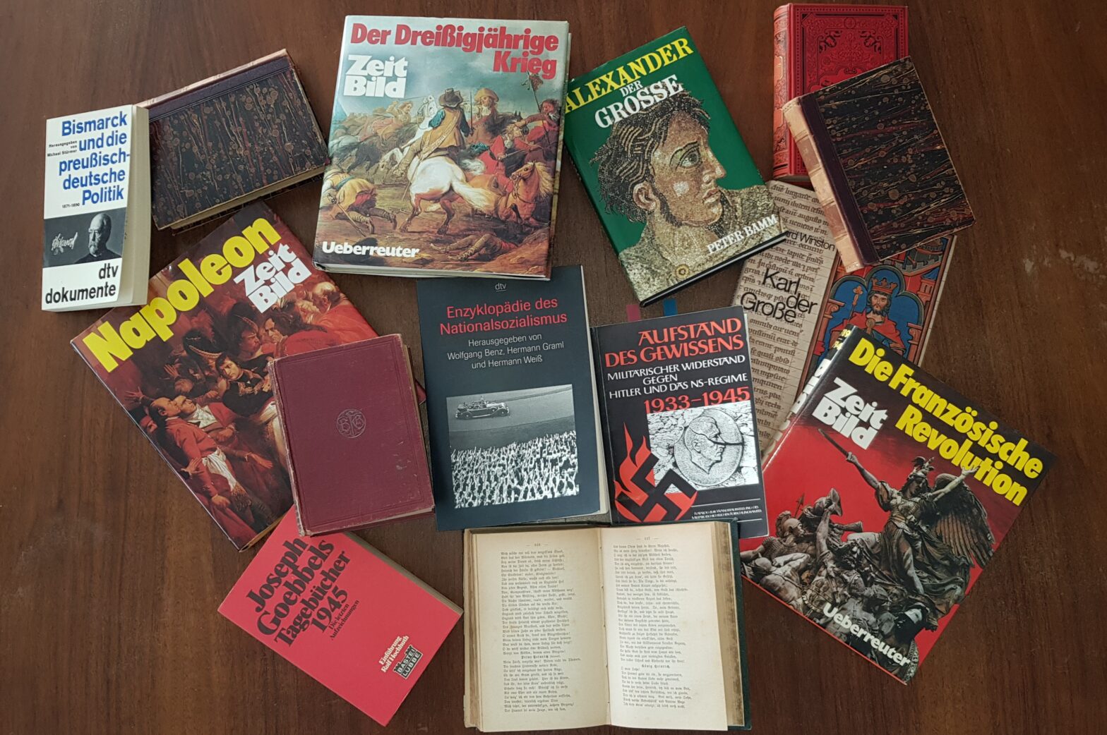 Mehrere deutschsprachige Geschichtsbücher verschiedener Epochen verteilt auf einem Holzboden